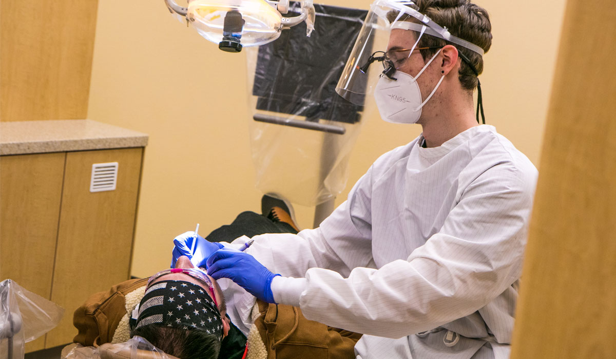 Patient sits in dental chair while Hygienest performs cleaning. 