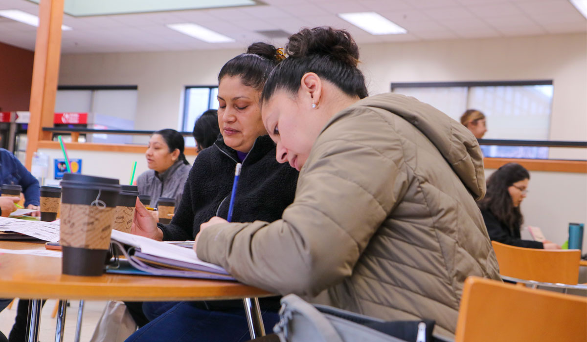 Two female students working in a note pad while drinking coffee.