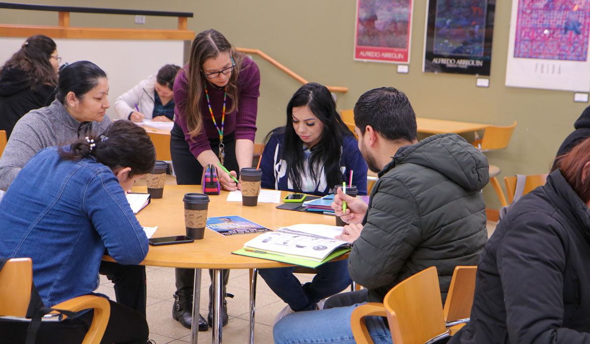 Instructor works with a group of students at a round table. 