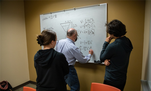 YVC instructor writes out math problem on the board while two students look on. 