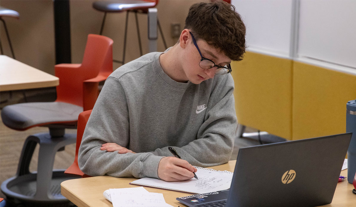 Student sits at a table working on his laptop. 