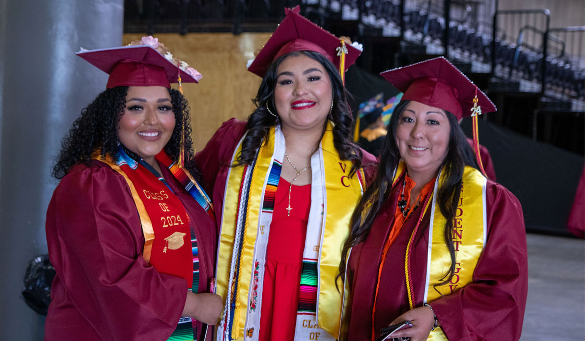 Three students pose for picture in their cap and gowns. 