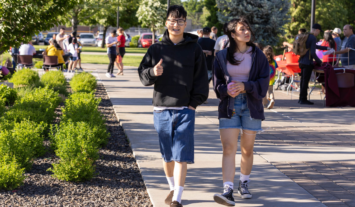 Male student gives thumbs up to the camera as he walks down the path. 