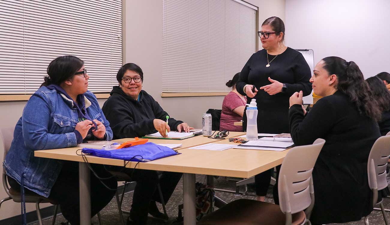 Female instructor stands next to table and talks to students