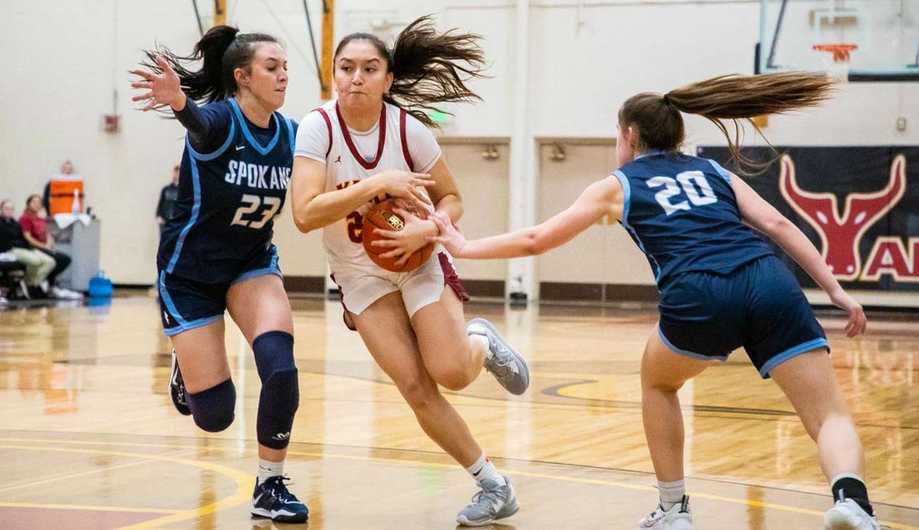 Female basketball player drives between two defenders