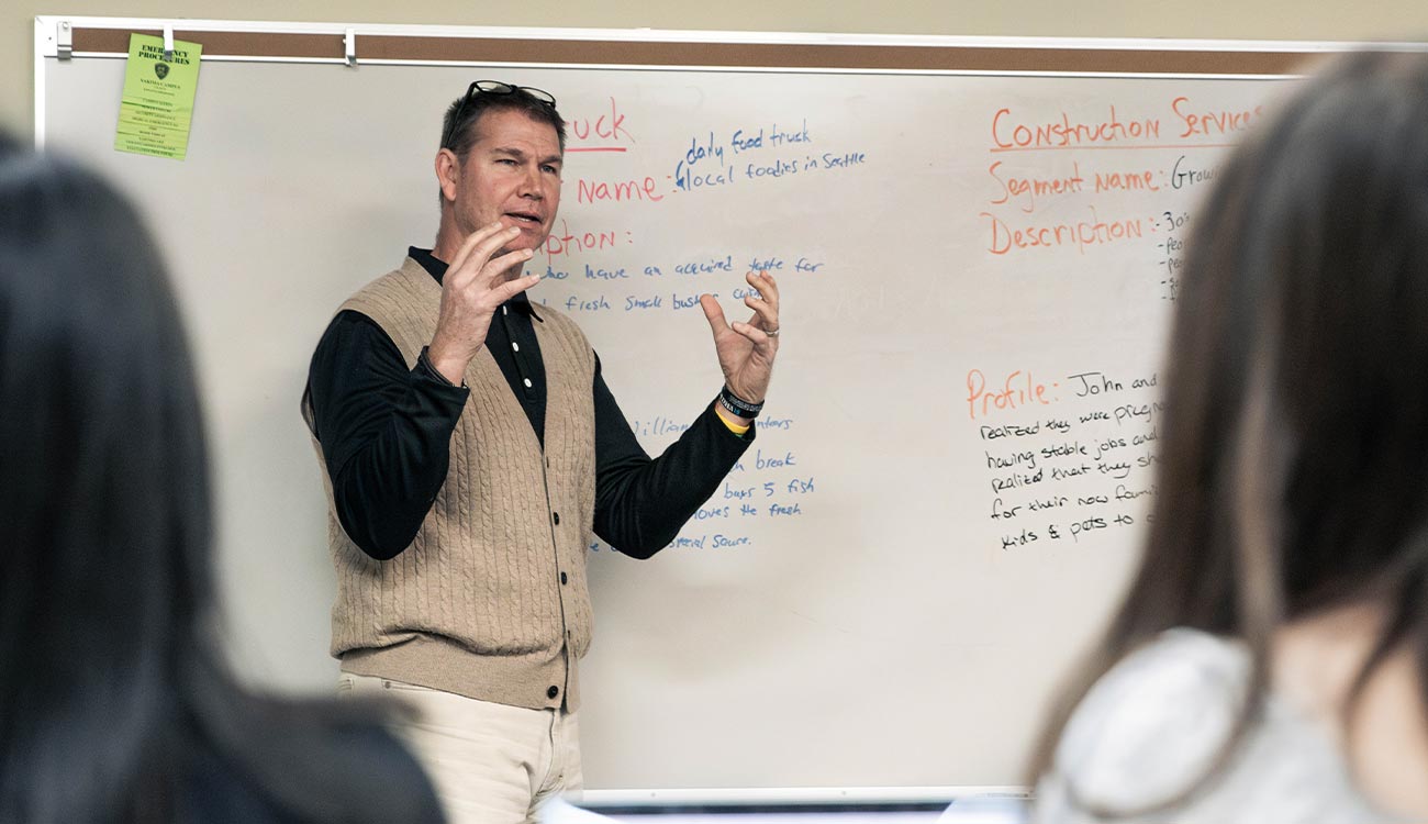 Business instructor in front of white board talking to students