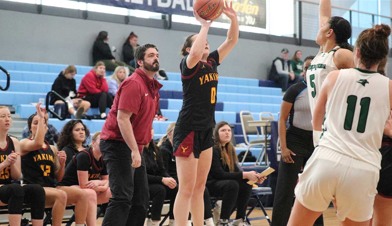 Female basketball player attempts jumpshot with coach in background