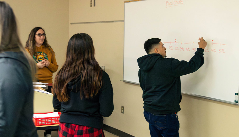 YVC Mathematics Instructor Michal Ramos looks at student writing math problem on white board