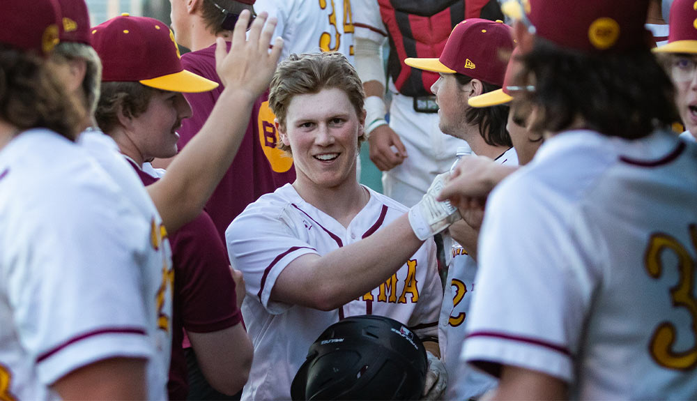 Yakima Valley College baseball player celebrates with teammates in dugout after scoring run