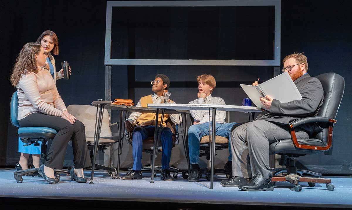 Five students sitting at a table performing during a YVC Drama Production. 