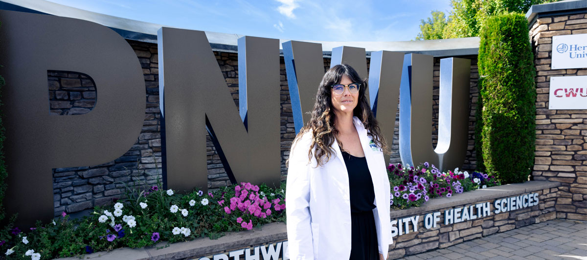 Staff member poses for picture in front of PNWU sign