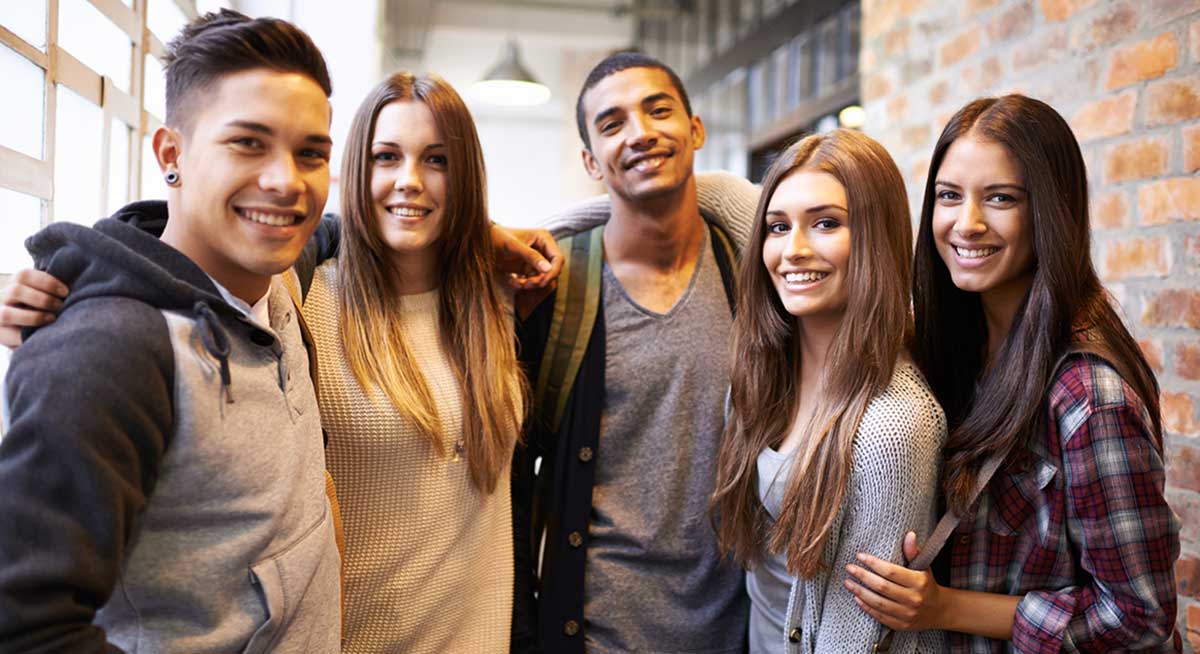 Group of five college students pose for picture with brick wall in the background