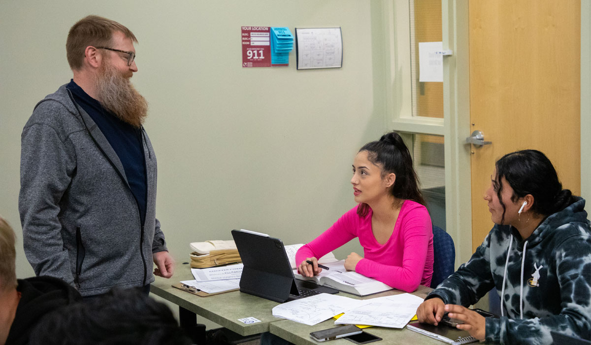 YVC Instructor speaks with two students on lap tops. 