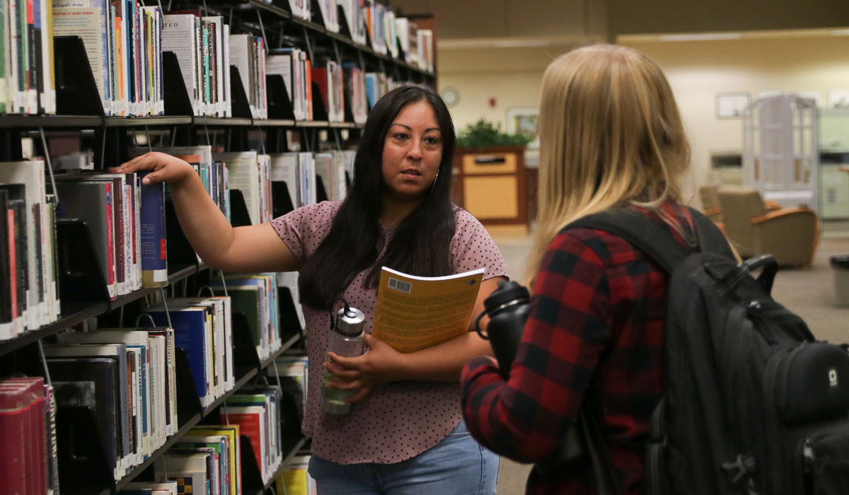 Two students talking in the YVC Library. 