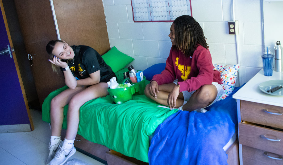 Students sitting on dorm bed. 