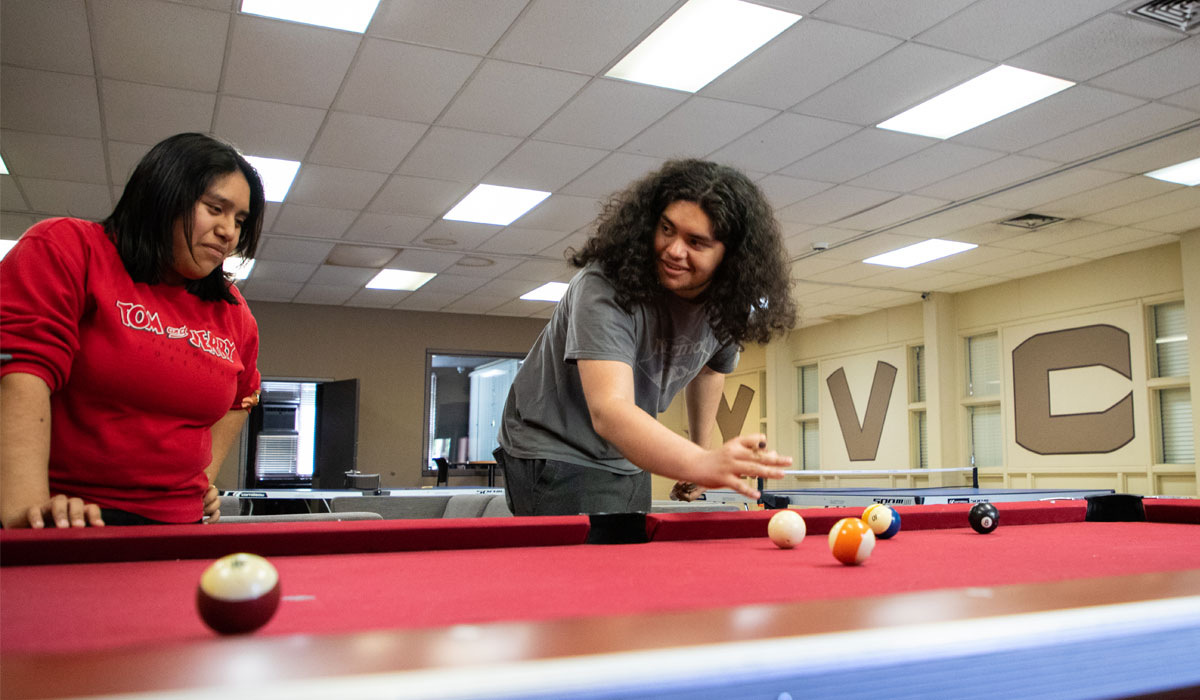 Two students playing pool on a red pool table. 