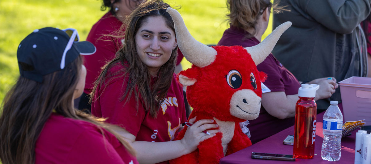 Two students sitting at a table during an event holding a stuffed animal yak. 