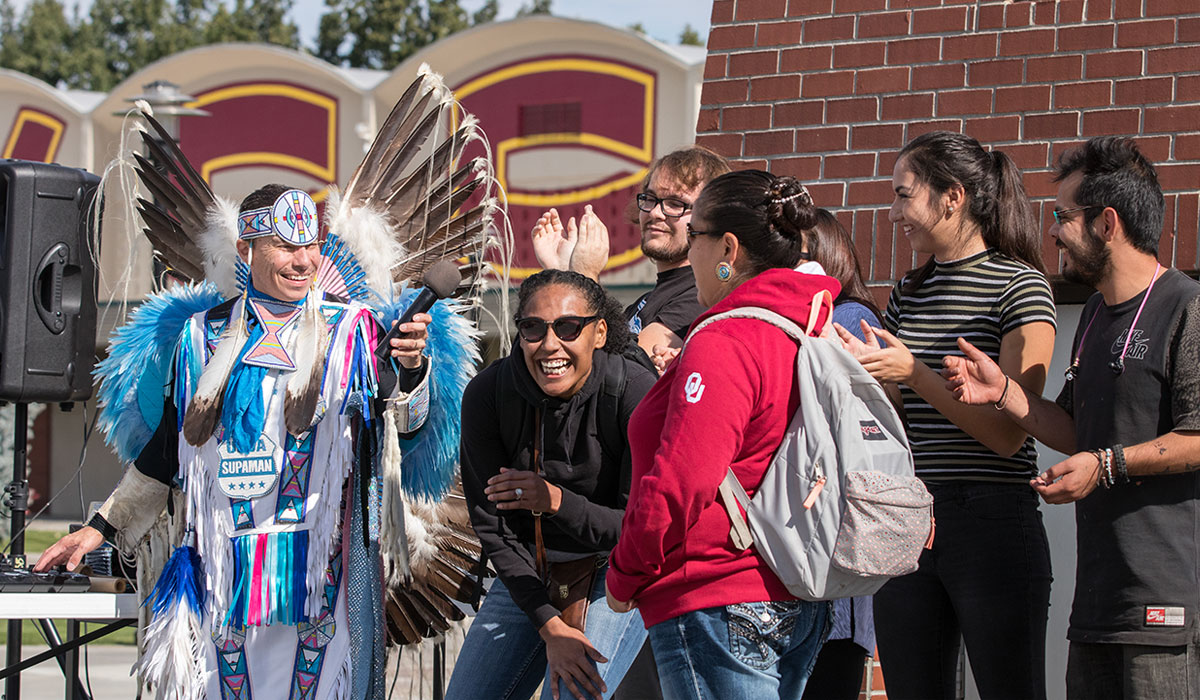 Guest speaker in traditional Native American outfit talks with students. 