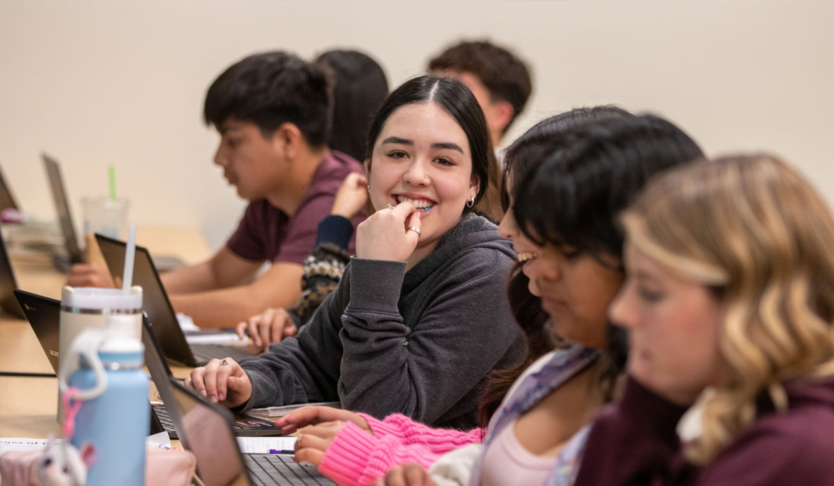 Girl smiles for camera while sitting amongst class mates. 