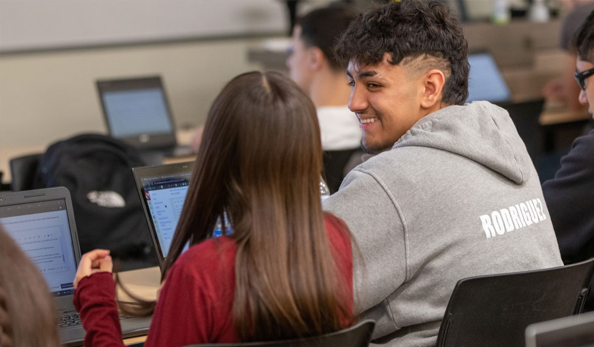 Two students sitting at computers laughing .