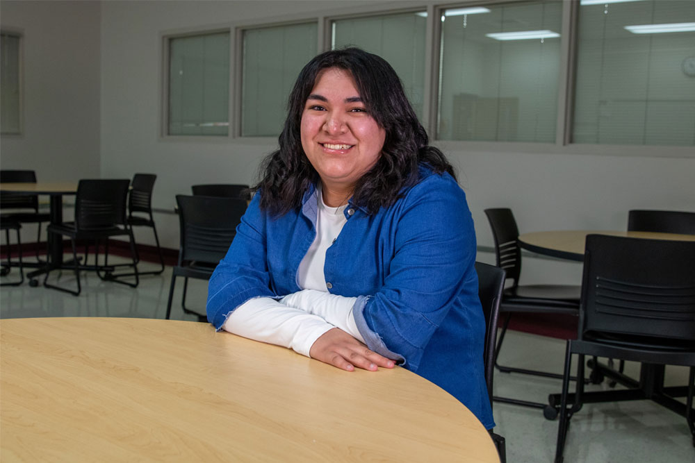 Jeanette Martinez poses for student story picture sititng at a table in a YVC classroom. 