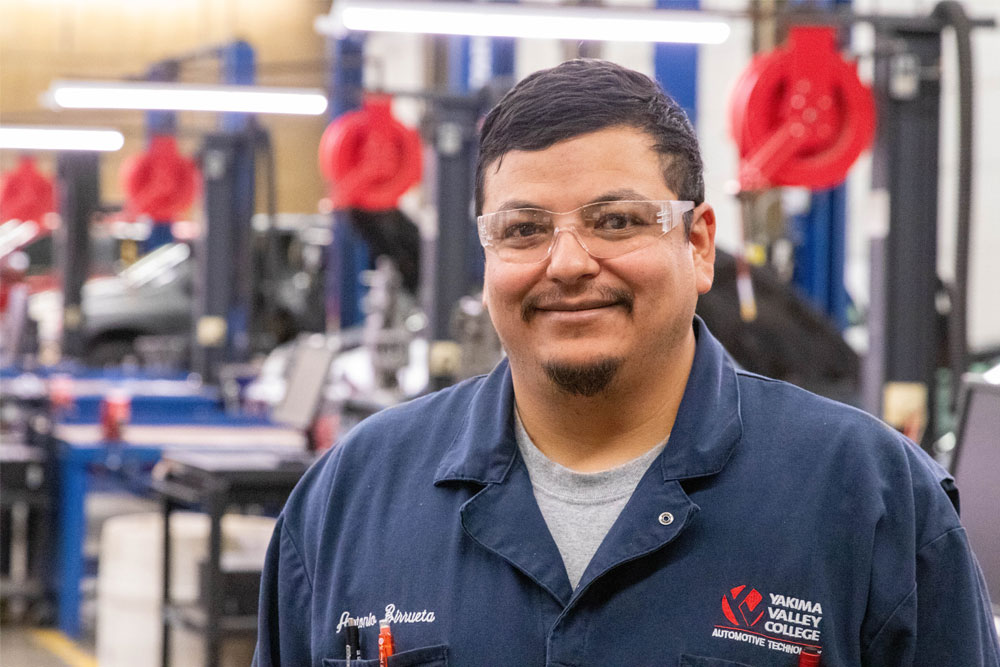 Antonio Biruetta pictured in his YVC Auto Tech uniform with the auto shop in the background. 