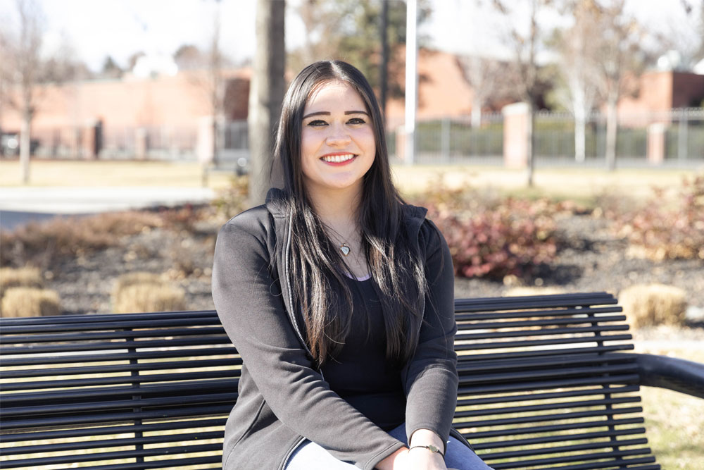 Diana Corona poses on a park bench for her student story picture. 