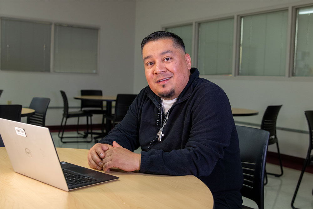 Eric Uribe poses for Student Story picture sitting at a desk with his lap top. 