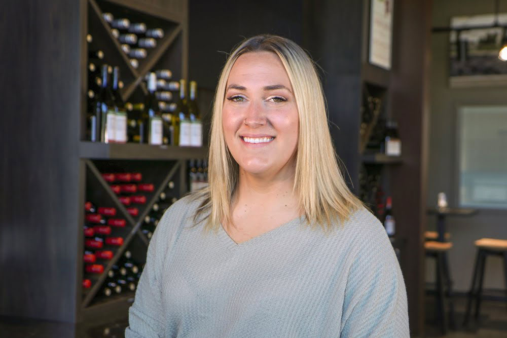 Samantha Mallery poses for Student Story Picture in front of a Wine Cellar. 