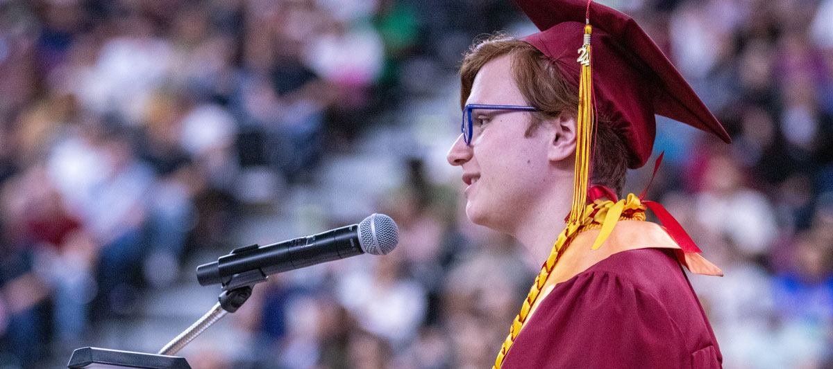 Student Speaker giving address at Commencement wearing red cap and gown. 