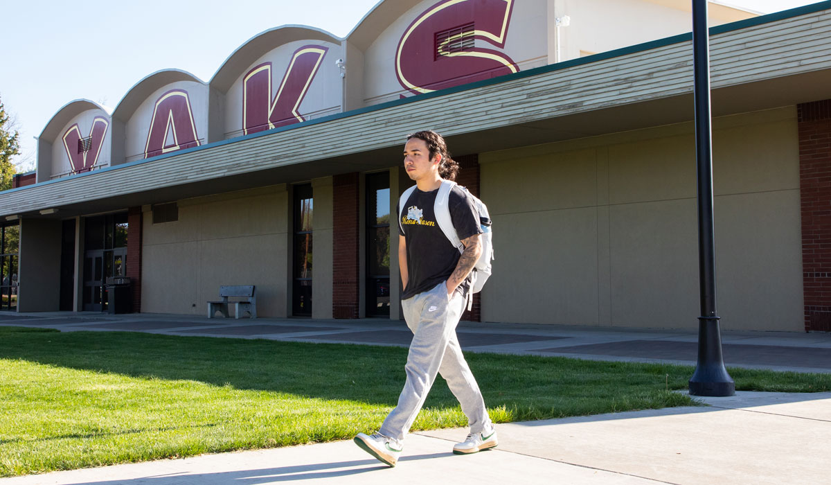 Student walks in front of building that has YVC painted in red behind him.