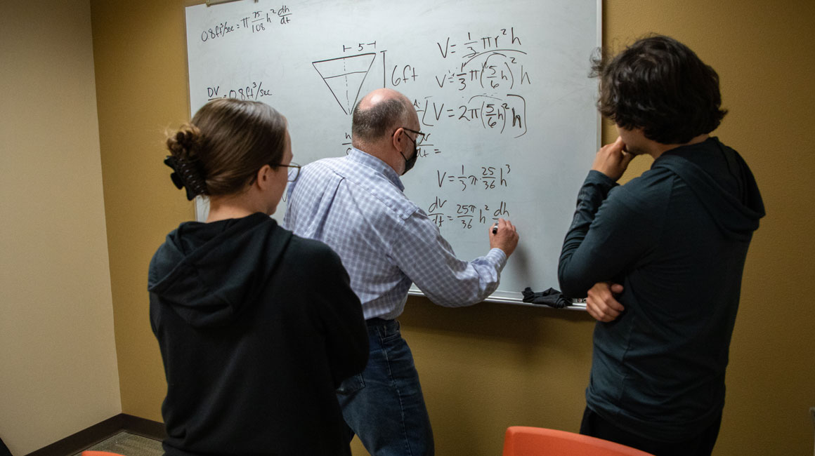 Math instructor writes problem on the board. 