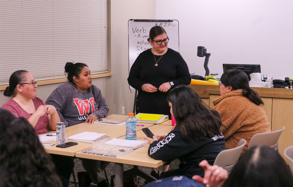 YVC instructor stands at a table of four students discussing class work.