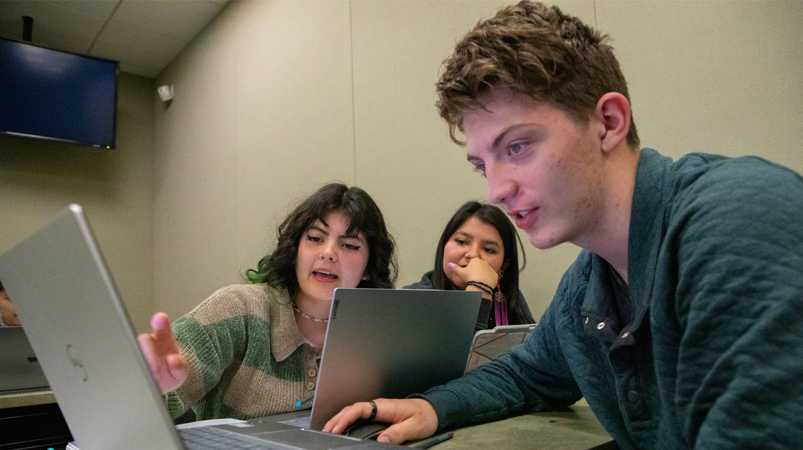 Student pointing to something on a classmates lap top during class.