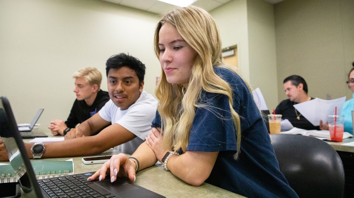 A student leans over to look at a classmates computer screen.